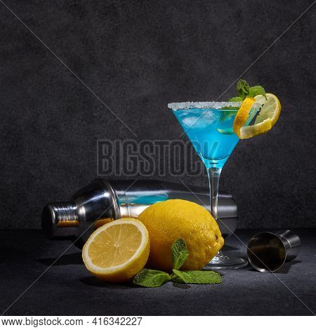 Glass with blue curacao cocktail, fresh mint and lemon, bar tools on dark grey background with copy space. Bar. Party. Blue cocktail.