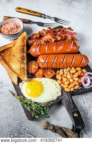 Full Fry Up English Breakfastt With Fried Eggs, Sausages, Bacon, Beans And Toasts On A Wooden Cuttin