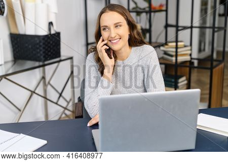 Smiling Young Female Entrepreneur Talking On The Smartphone Sitting At The Desk, Cheerful Woman Has 