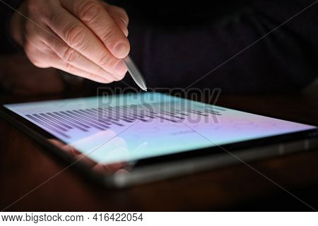 Male Hand Holds Stylus Over Screen Of Tablet With Commercial Charts In Dark