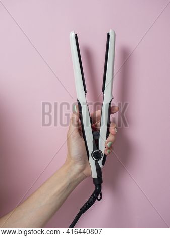 White Curling Iron In A Woman's Hand On A Pnk Background. An Accessory For Creating Hairstyles. Beau