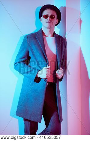 Porttrait of a handsome middle-aged man in an elegant coat and a hat standing by a white wall and smiling. Men's beauty, fashion. Lifestyle. Hipster man. 