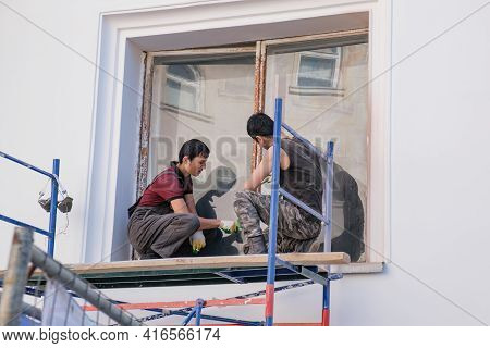 Moscow, Russia 04.11.2021 Two Asian Workers Cleaning The Window Frame With The Outside Of The Buildi