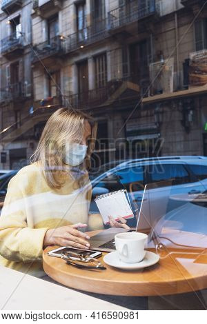 Young Blond Woman With A Face Medical Mask Working With Laptop In Cafe. Writing. Online Courses, Stu
