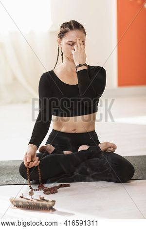 A Woman In Black Sportswear Sitting On A Mat In A Lotus Position, Is Engaged In Meditation And Breat
