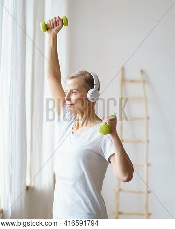 Portrait Of Smiling Senior Woman Exercising Fitness With Dumbbells At Home. Mature Female Build Up B