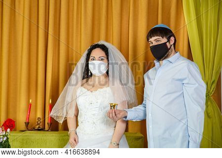During The Chuppah Ceremony In The Synagogue, The Bride And Groom Stand Next To The Groom Holding A 
