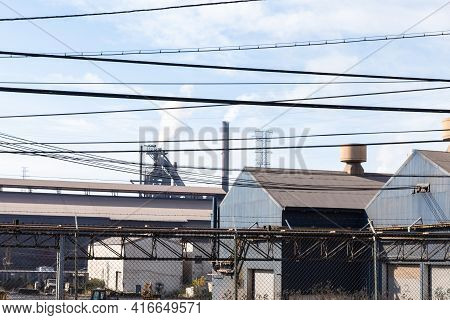 Criss Cross Of Power Lines Before A Working Steel Mill, Blast Furnaces And Large Warehouse Buildings