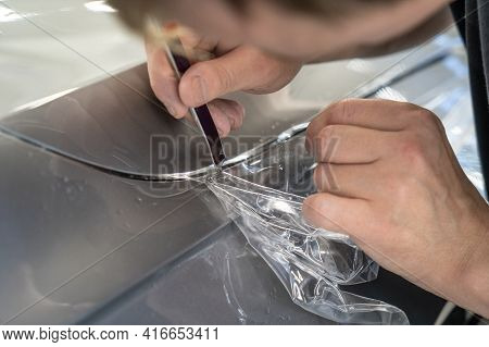 Detailer Worker Cuts With Knife Wrapped And Installed Ppf For Car Protection Film On Vehicle Hood.