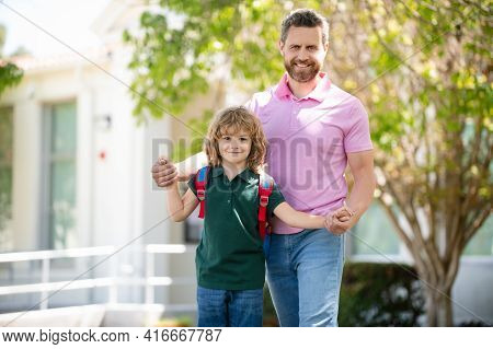 American Father And Son Walking Trough School Park. Parent Leads A Little Child School Boy In First 