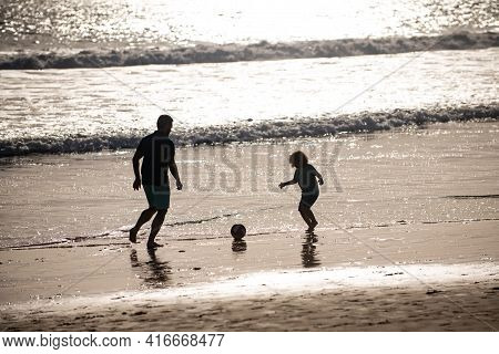 Father And Son Play Soccer Or Football On The Beach On Summer Family Holidays. Dad And Child Having 