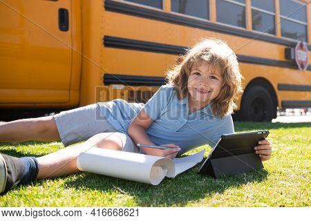 Portrait Of Little Schoolboy Writing Outdoor In School Park And Doing Homework