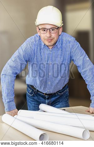 An Engineer With Glasses And A Construction Helmet Bent Over The Table With Documents. Making Change