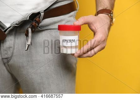 Donor With Unzipped Pants Holding Container Of Sperm On Yellow Background, Closeup