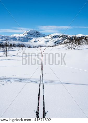 Skis Stacked Together In The Snow With Blurred Snow Capped Mountains.
