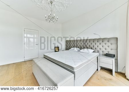 Modern Bed With Comfortable Mattress And Soft Pillows Located Near Bedside Table And Electric Firepl