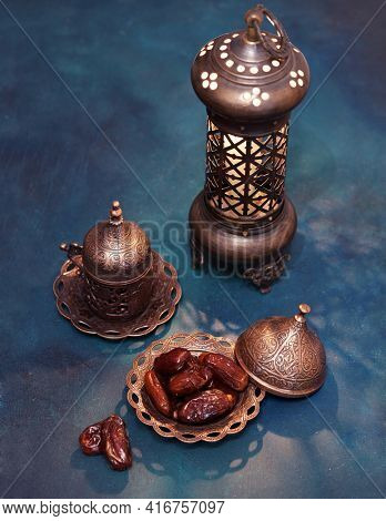 Bronze plate with dates, coffee cup, arabic lantern  on dark blue-green painted  wooden background.  Ramadan background. Toned image