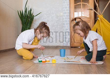 Two Children In Light Clothes Sit On The Floor On Their Knees And Enthusiastically Draw With Bright