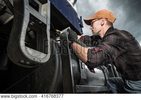 Semi Truck Driver In His 40s Checking Vehicle Elements Near Fuel Tank. Heavy Duty Transportation The