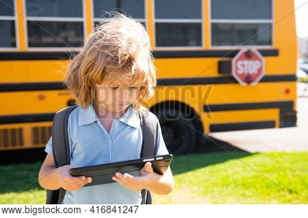 Child Does School Homework With Tablet In The Park Near School Bus. School Kid Outdoor