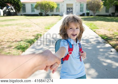 Father Leads A Little Child School Boy In First Grade. Little Boy With Backpack Holding Parent Fathe