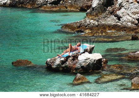 Young girl is sunbathing on a rocky beach in Croatia