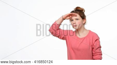 Portrait Of A Curious Young Girl In Pink Casual Sweatshirt Looking Far Away With Hand At Her Forehea