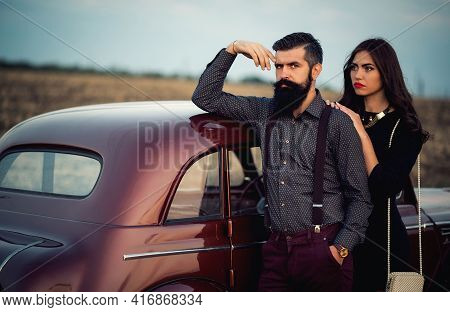 Bearded Brunette Man In A Shirt And Trousers With Suspenders Hugs A Slender Young Girl With Long Hai