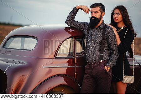 Stylish Bearded Brunette Man In A Shirt And Trousers With Suspenders Hugs A Slender Young Girl With 