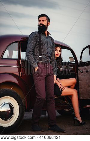 Stylish Bearded Brunette Man In A Shirt And Trousers With Suspenders Hugs A Slender Young Girl With 