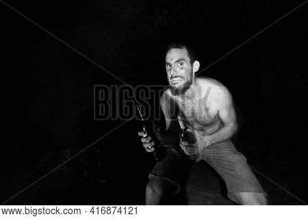 Wild man grabbing bottle in the dark by a campfire, uncivilized look
