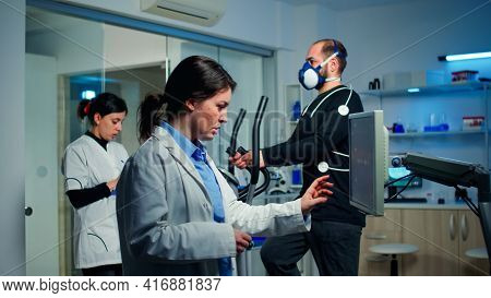 Doctor Sport Scientist Checking Ekg Scan At Monitor While Man With Mask Running