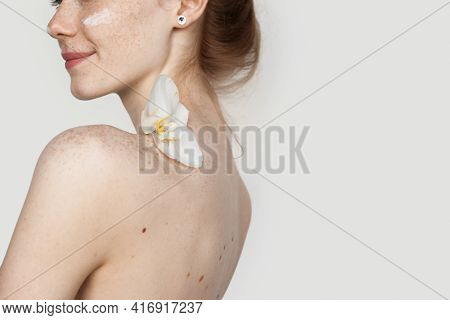 Caucasian Woman Applying Cream On Her Cheeks Is Smiling Holding A Flower On Her Empty Shoulders