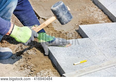 A Worker In A Blue Overalls, Half Crouching, Knocks With A Rubber Hammer On Granite Blocks, Assembli