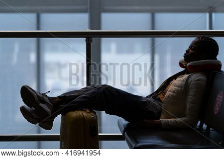 Tired Woman Sleep In Airport On Chair With Legs On Suitcase Waiting For Transit Flight Departure. Bl