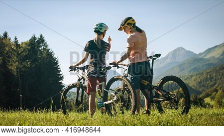 Two Females On Mountain Bikes Talking And Looking At Beautiful Green Nature.