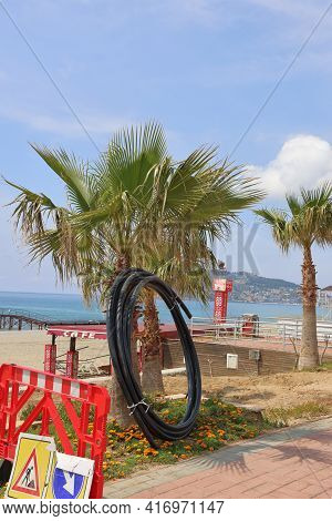 Alanya, Turkey, April 14, 2021. A Pipe Twisted In A Ring Leaning Against A Palm Tree On The Frn Of T