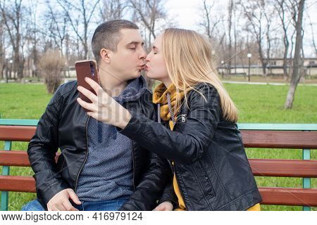 Husband And Wife Take A Selfie While Sitting On A Swing In The Park. Happy Couple Taking Pictures Of