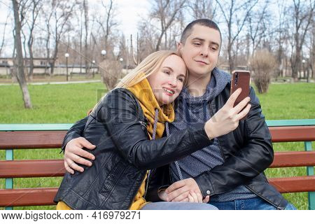 Husband And Wife Take A Selfie While Sitting On A Swing In The Park. Happy Couple Taking Pictures Of