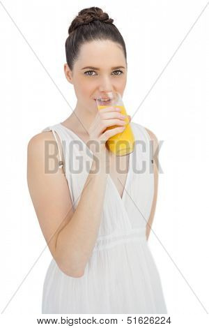 Cheerful model in white dress drinking orange juice while posing on white background