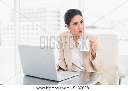 Smiling businesswoman holding mug while working on laptop at the office