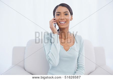 Cheerful attractive woman on the phone sitting on cosy sofa in bright living room