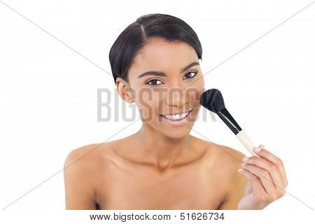 Smiling natural model using blusher brush while posing on white background