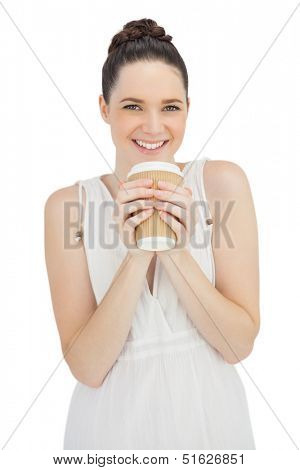 Smiling natural model in white dress drinking coffee while posing on white background