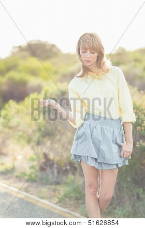 Gorgeous blonde woman hitchhiking on the road on a glowing background