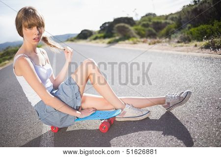 Pouting funky blonde sitting on her skateboard on a deserted road