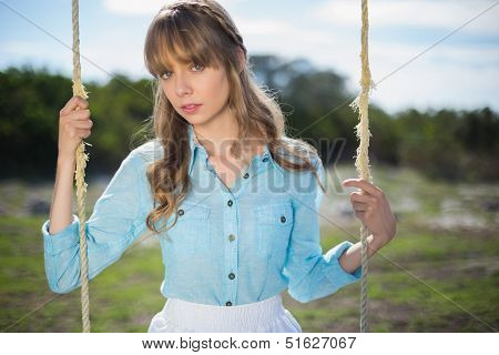 Mysterious young model relaxing in a sunny garden sitting on swing