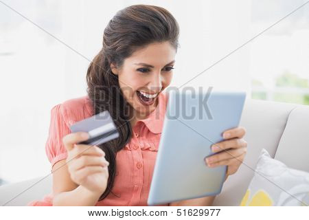 Ecstatic brunette sitting on her sofa using tablet to shop online at home in the sitting room