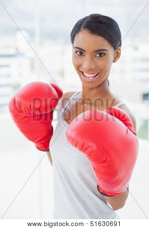 Competitive cheerful model wearing red boxing gloves in bright room at home