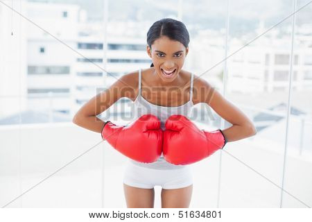 Competitive model wearing red boxing gloves in bright room at home